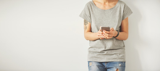 Naklejka premium Beautiful hipster woman checking email via mobile phone while background with copy space for text message or promotional content, charming female holding cell telephone in hands while waiting friends.