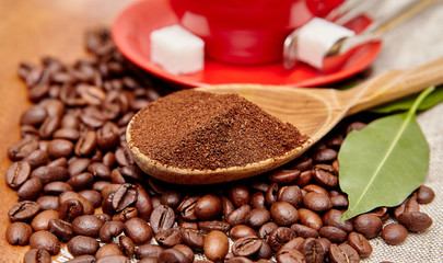 Natural ground coffee heap in a wooden spoon on a background of coffee beans and red cup