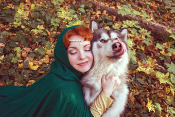 A fairytale fantasy. Red-headed woman in autumn forest. She dressed in renaissance costume. With dog