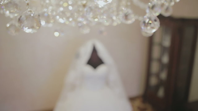 Elegant white wedding dress near the crystal chandelier.