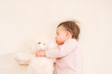 Amazing portrait of sleeping beautiful baby toddler girl with a fluffy teddy bear on the bed