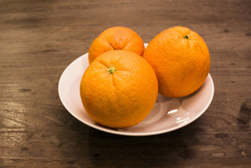 three oranges in white porcelain bowl on wood table