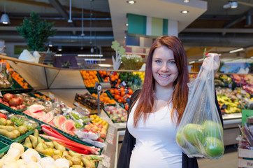 Pregnant woman with green apples in polybag hold in supermarket