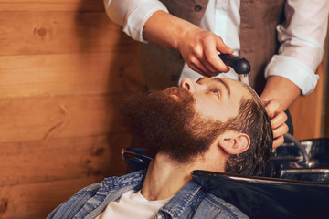 Barber washing head of bearded man