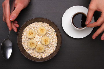 Woman hands holding spoon, healthy breakfast - eggs, black coffee and Oats flakes with banana. Whole grain cereal.