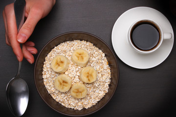 Woman hands holding spoon, healthy breakfast - eggs, black coffee and Oats flakes with banana. Whole grain cereal.