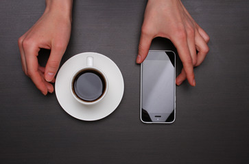 Fototapeta premium Woman hands touching smart phone and holding coffee cup. Top view