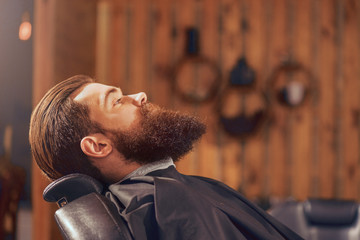 Pleasant man sitting in the barbershop - obrazy, fototapety, plakaty