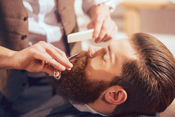 Professional barber cutting beard of handsome man - obrazy, fototapety, plakaty