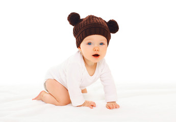 Baby in knitted brown hat with ears bears crawls on white backgr