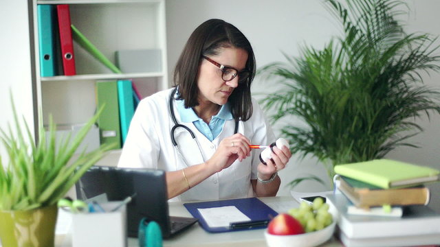 Doctor working on papers in her office and checking a drug
