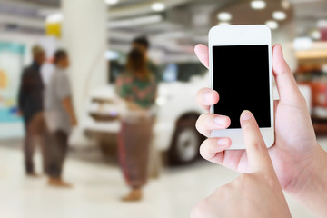 hands holding mobile phone with new cars in showroom