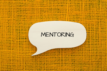 Mentoring message written on a paper on burlap background.