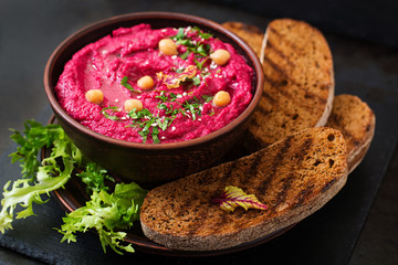 Roasted Beet Hummus with toast in a ceramic bowl on a dark background