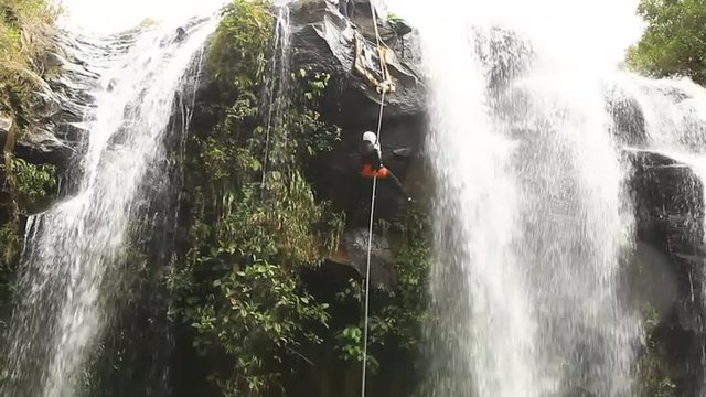 Experience the breathtaking beauty of an Ecuadorian rainforest as you witness an awe inspiring wide angle shot capturing a fearless individual rappelling down a majestic waterfall.