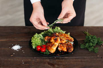 Food decoration on wooden table. Chief presents grilled spicy chicken. Decorating chicken wings with lettuce and tomatoes cherry. 
