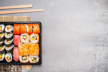 Sushi rolls and chopsticks on gray stone background, top view, place for text.
