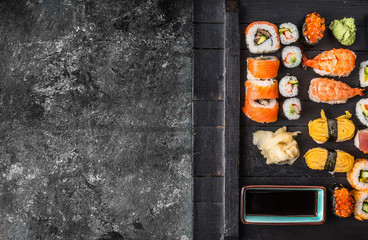 Various sushi on black wooden plate on rustic grunge background, top view, border