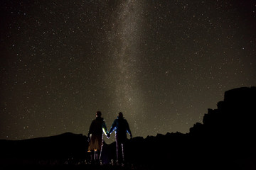 Obraz na płótnie Canvas Couple is standing in mountains against night sky with milky way