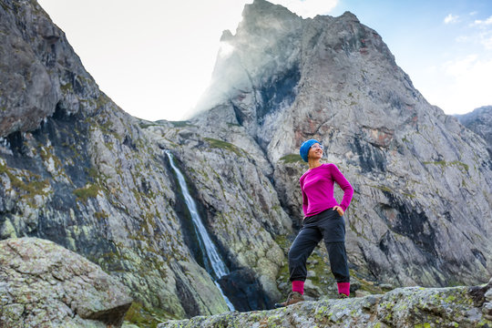 Woman trekker is standing against high mountains waterfall in Ca