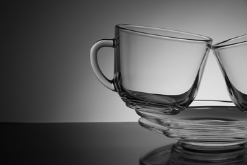 Two glass cup for tea and an empty saucer on a black background