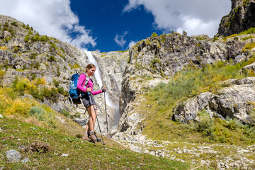 Fototapeta premium Woman trekking in Caucasus mountains against high waterfal in Us