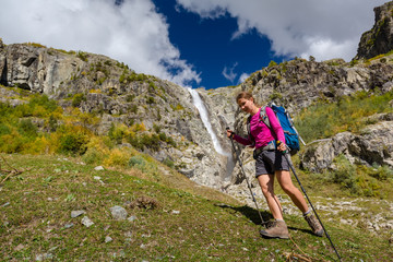 Fototapeta premium Woman trekking in Caucasus mountains against high waterfal in Us