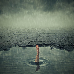 Surrealistic image with a single hand of drowning man asking for help in a pothole of cracked...