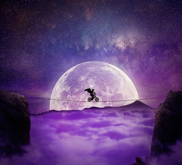 Boy with angel wings balance on a wire over a chasm riding a bicycle. Self overcoming and risk...