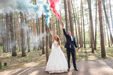 The bride and groom  with   smoke bombs on the background of trees