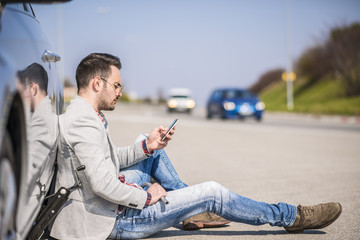 Young man with a silver car that broke down on the road