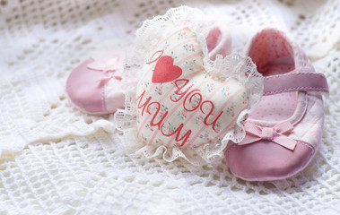 Textile handmade white heart with the inscription I love mum and little pink baby shoes on a white knitted napkin
