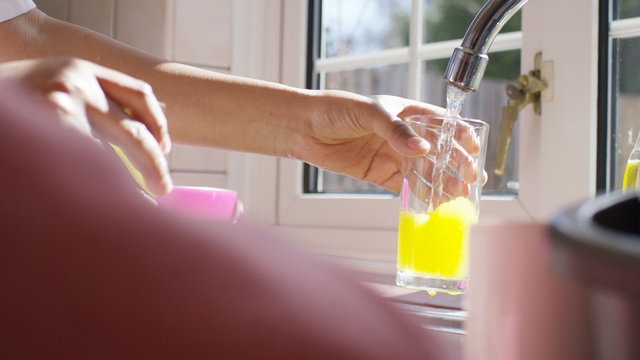 Grown up hands filling a glass of orange squash from a kitchen tap, in slow motion