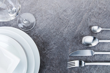 Teller und Besteck aus Edelstahl und Glas angeordnet auf einer schwarzen Granitplatte in Draufsicht