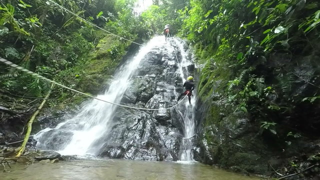 Experience the thrill with slow motion footage of Asiatic men tourists engaging in exhilarating waterfall rappelling adventure.