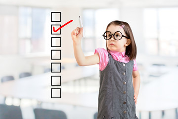 Cute little girl wearing business dress and checking on checklist box. Office background.
