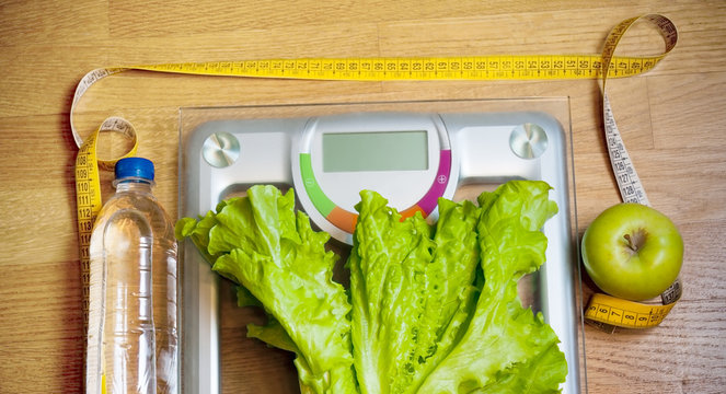 Bottle of water, salad, green apple,  yellow measuring tape and weight scale. Dieting concept.