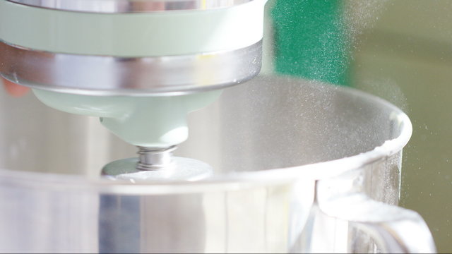 Mixing machine mixes ingredients as fine caster sugar dances around the edge of the bowl, in slow motion 