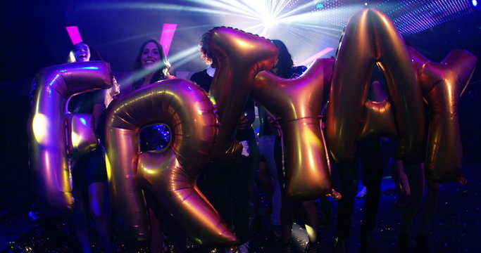 Group of friends dancing in a nightclub holding FRIYAY balloons