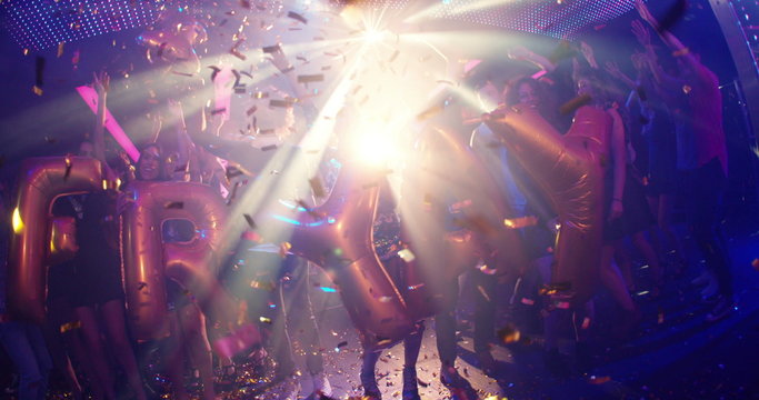 Group of friends dancing in a nightclub holding FRIYAY balloons