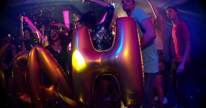 Party friends in night club with yeah balloons and confetti