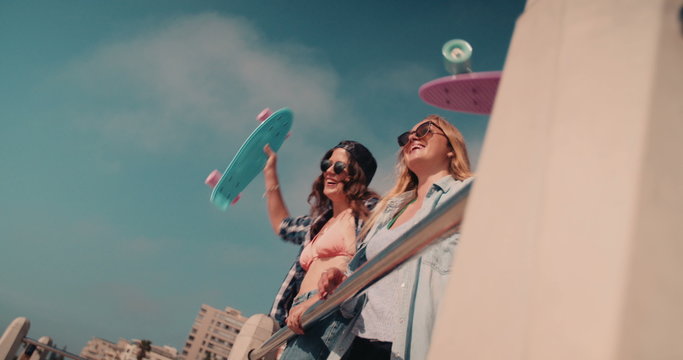 Teen girl friends at the beach lifting their skateboards up 