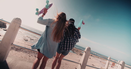 Hipster girls with skateboards on summer day at the beach