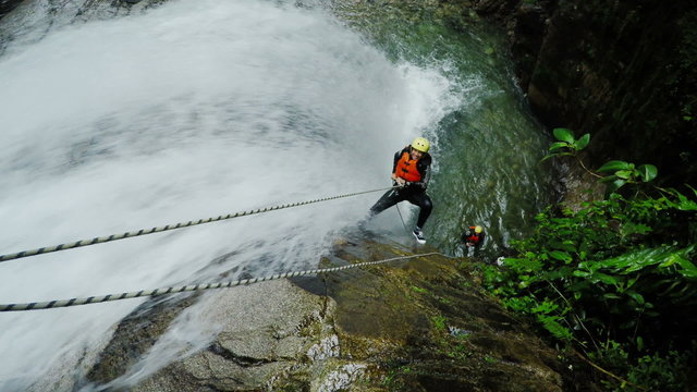 real-time action shot of two tourist rappelling thru tall waterfall static camera with sound background voices sprint race visitors team dual nature work outside falls group crowd pair canyoning outd