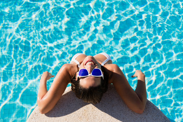 Top view of funny woman enjoying summer vacation in resort swimming pool. Beautiful brunette girl wearing sunglasses and having fun on summertime.
