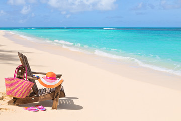 Fototapeta na wymiar Chair with bag, hat, flip-flops and sunglasses on sunny beach, summer ho;day concept