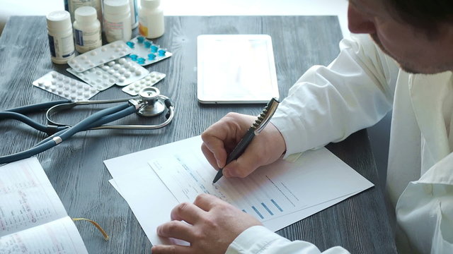 Male doctor writing rx prescription at the table use tablet