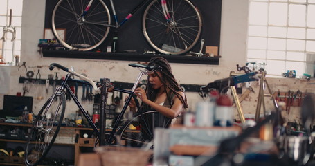 Afro woman bicycle mechanic recpairing a bike in her workshop - Powered by Adobe