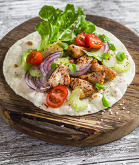 Delicious grilled chicken and fresh vegetables homemade tortilla on a rustic cutting board on a light wooden background