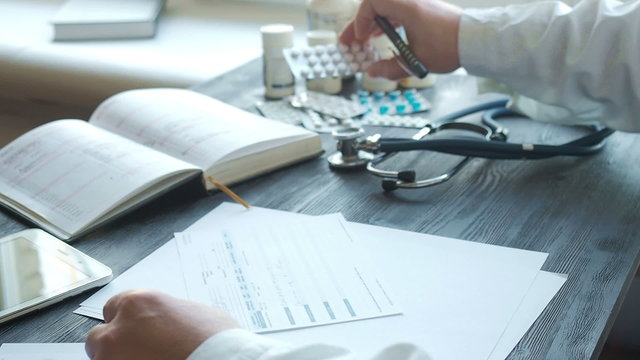 Male doctor writing rx prescription at the table watch medications